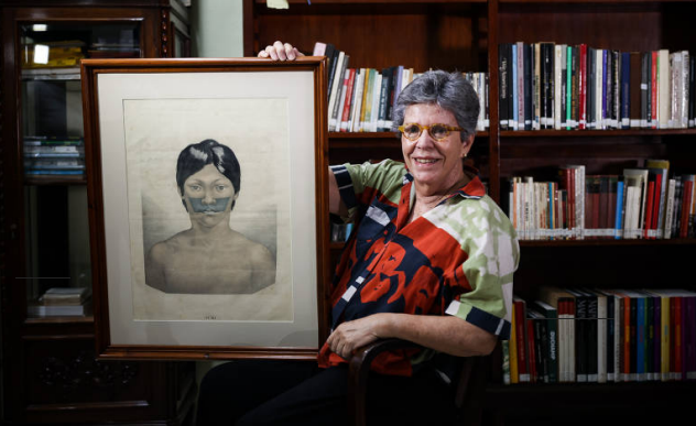 Professora Sylvia segurando um quadro com a imagem de um indígena 